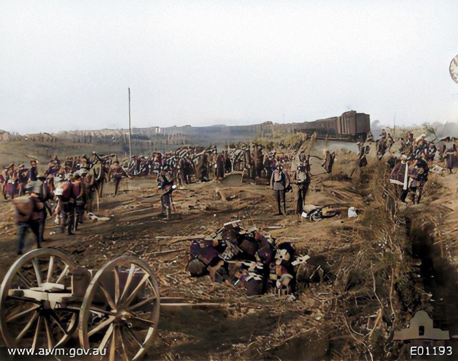 British troops entraining at the Poperinghe Gate, at Ypres, for the journey by train to a rest area after the fighting in the Third Battle of Ypres. In the left foreground there is a damaged limber and to the right is a pile of barbed wire rolls.